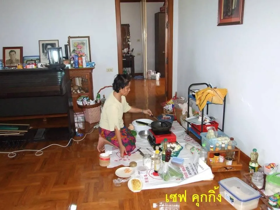 ผู้หญิงนั่งทำอาหารบนพื้นบ้านด้วยเตาปิกนิก