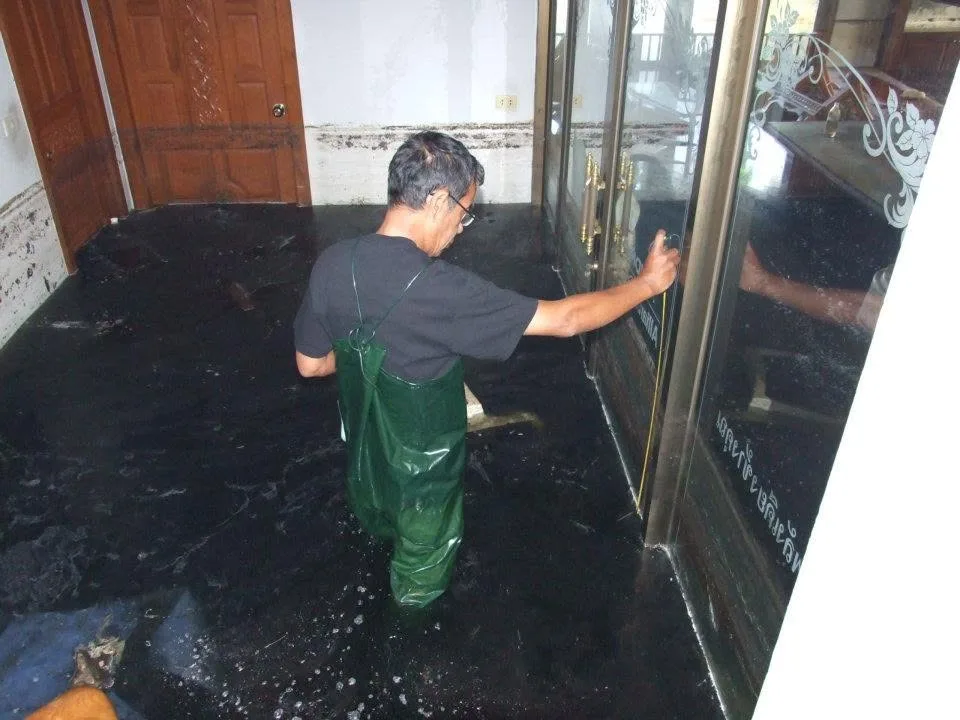 ชายสวมกางเกงยางลุยน้ำในบ้านที่ถูกน้ำท่วม